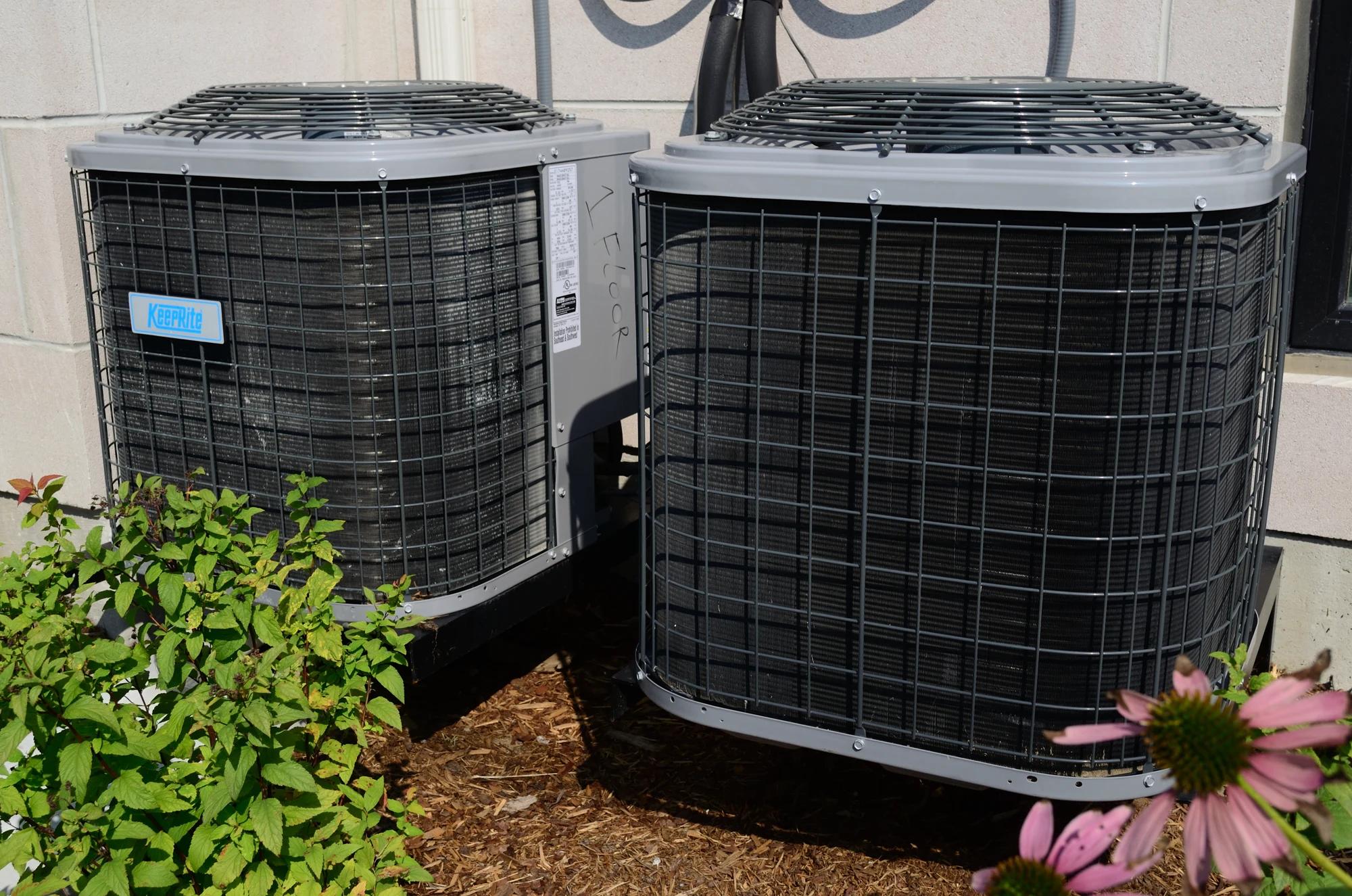 Two outdoor air conditioning condensing units standing beside a building wall