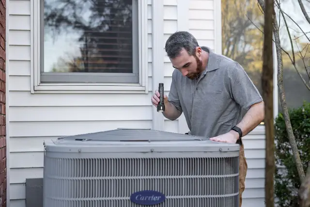 Technician inspecting a central air conditioner condenser beside a house