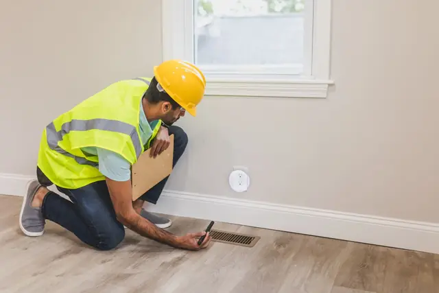 Worker checking airflow at a floor vent