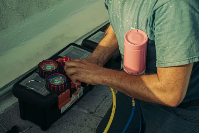 Technician holding a refrigerant gauge set beside an AC unit