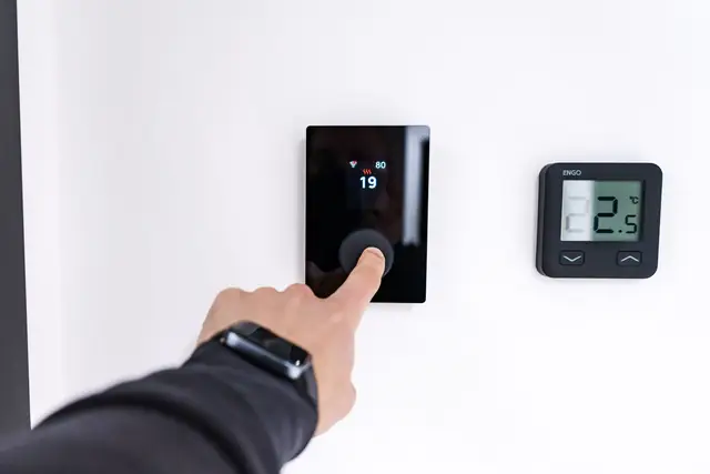 Person setting a digital thermostat on a white wall