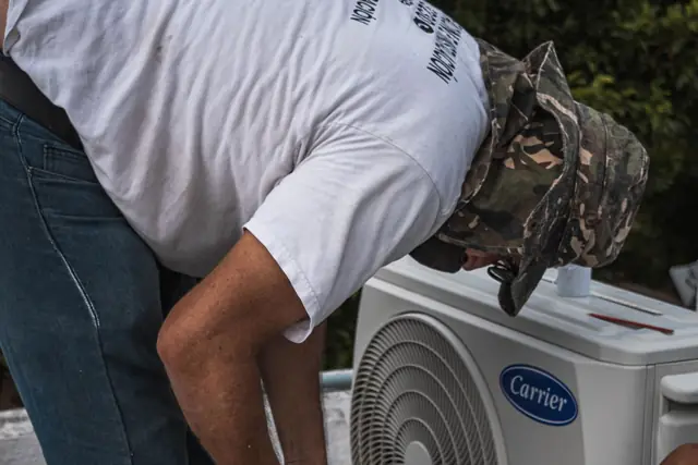 Technician bending over an outdoor AC unit to check the lines